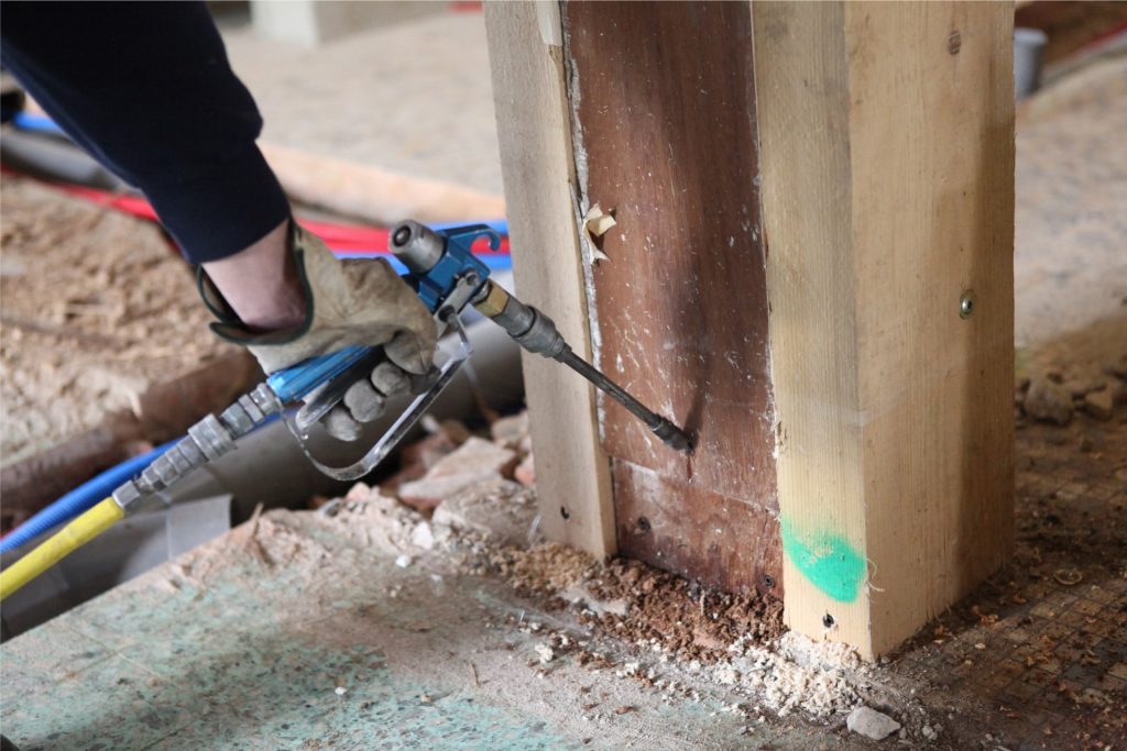 Technician injecting termite treatment into wooden structure to eliminate infestation