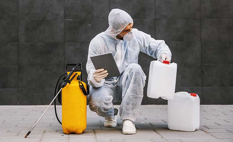 A technician in protective gear checks chemical containers while holding a tablet