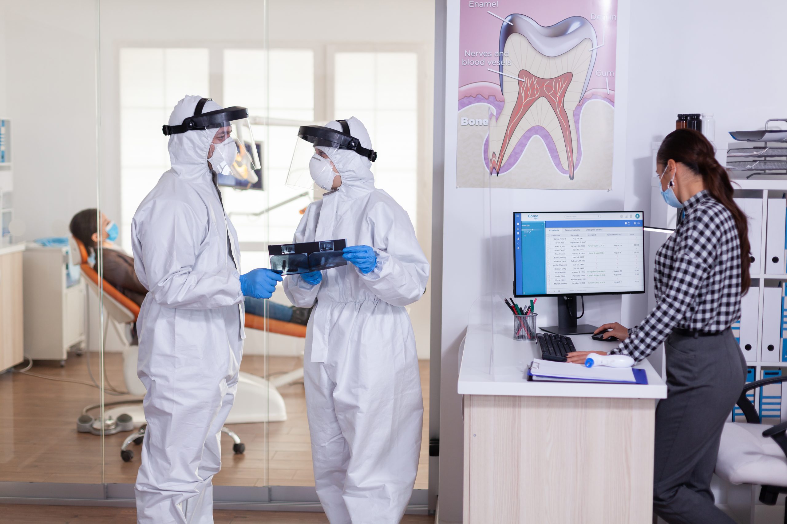 Two dental staff members in full PPE suits reviewing an x-ray inside a healthcare office – pest control for offices and medical facilities