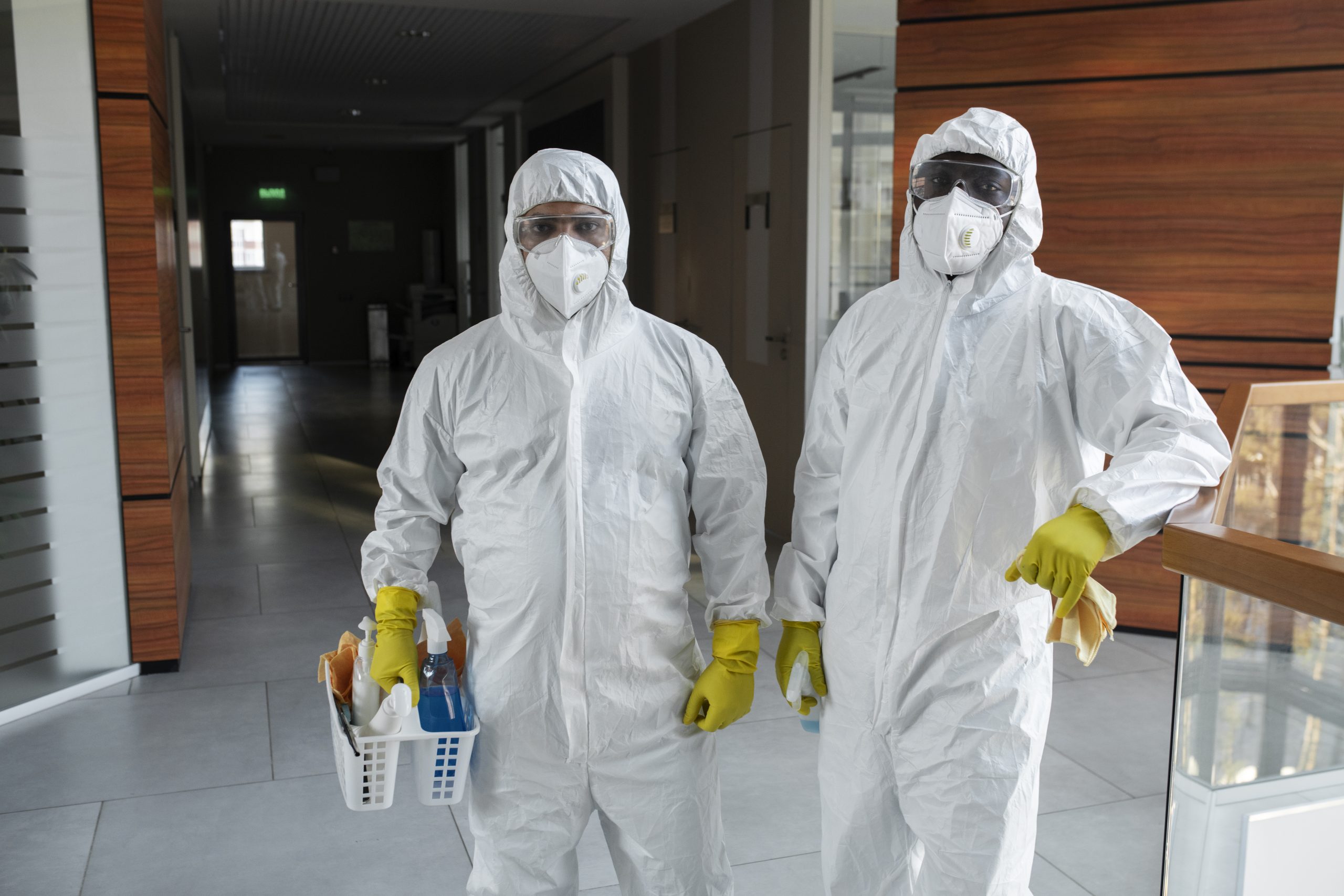 Two pest control professionals in protective suits holding cleaning supplies ready for school disinfection – school pest control team