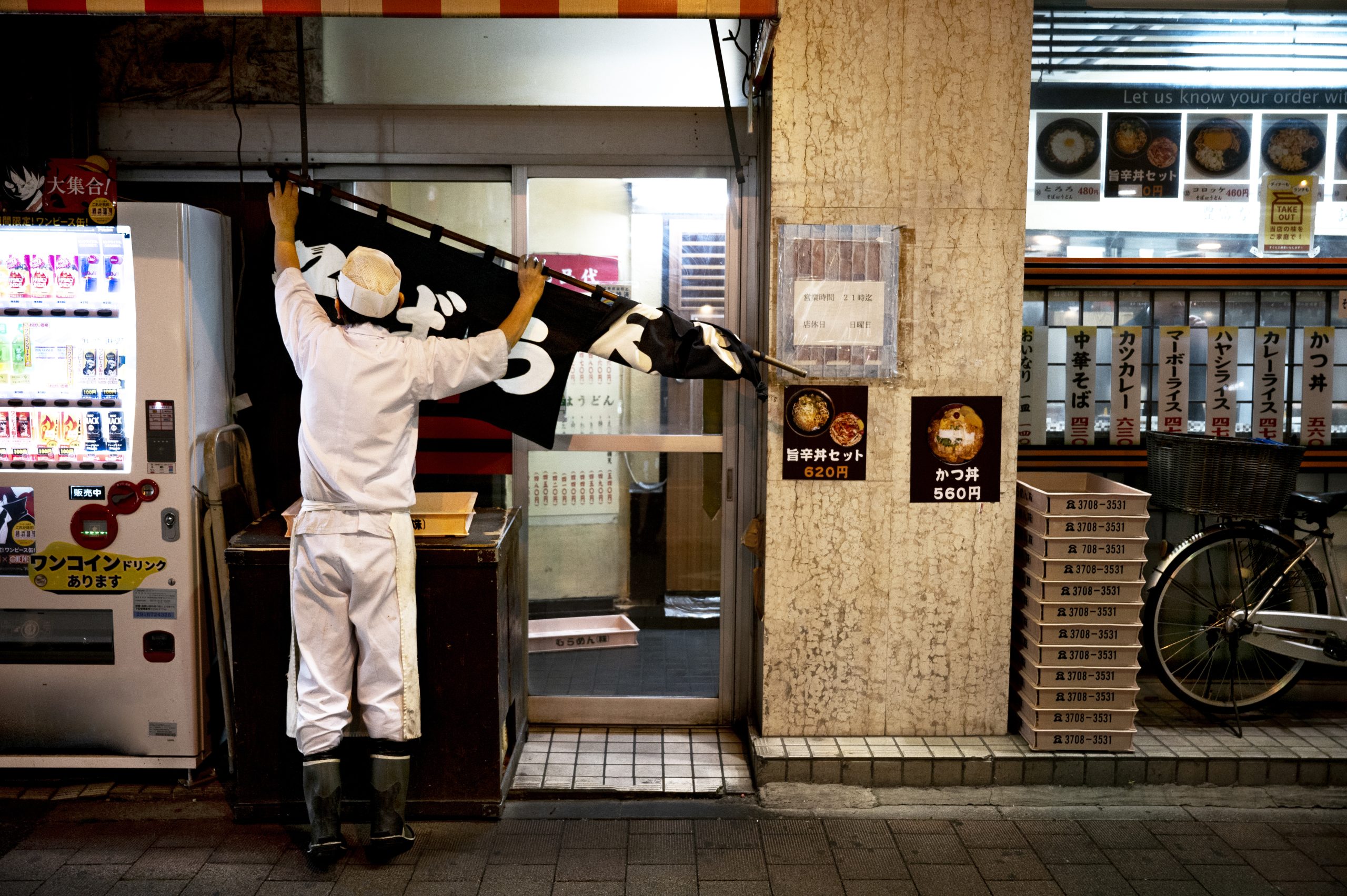 Worker in white uniform hanging signage outside a Japanese retail restaurant at night – restaurant and retail pest control services