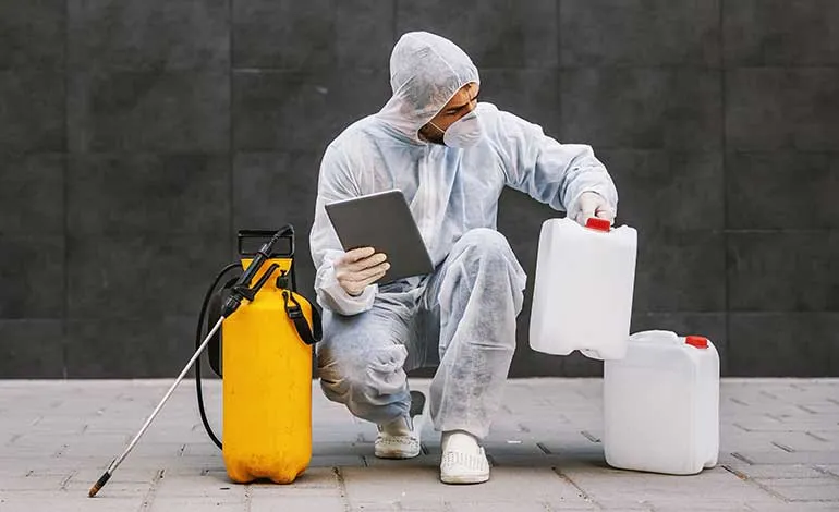 Technician in protective gear checks chemical containers while holding a tablet