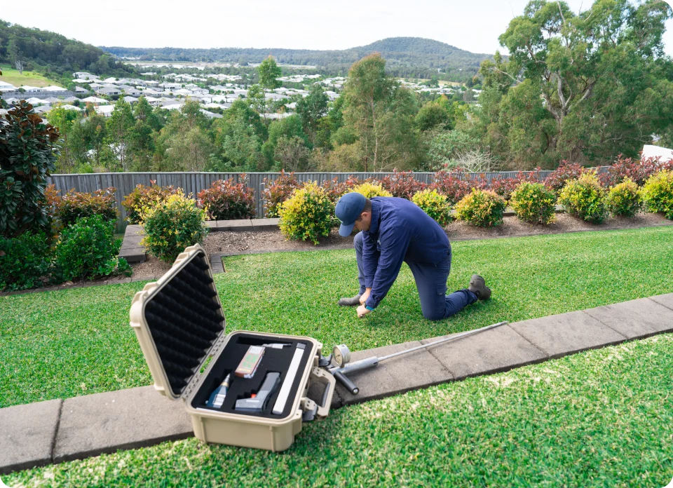 Technician inspecting a lawn for pests with tools and a field kit open nearby.