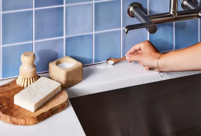 Hand sprinkling baking soda on a bathroom countertop.